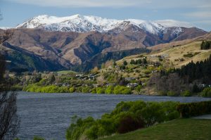 רכס ההרים The Remarkables המושלג מעל עמק ירוק ובתי מגורים בקווינסטאון, ניו זילנד