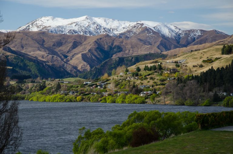 רכס ההרים The Remarkables המושלג מעל עמק ירוק ובתי מגורים בקווינסטאון, ניו זילנד